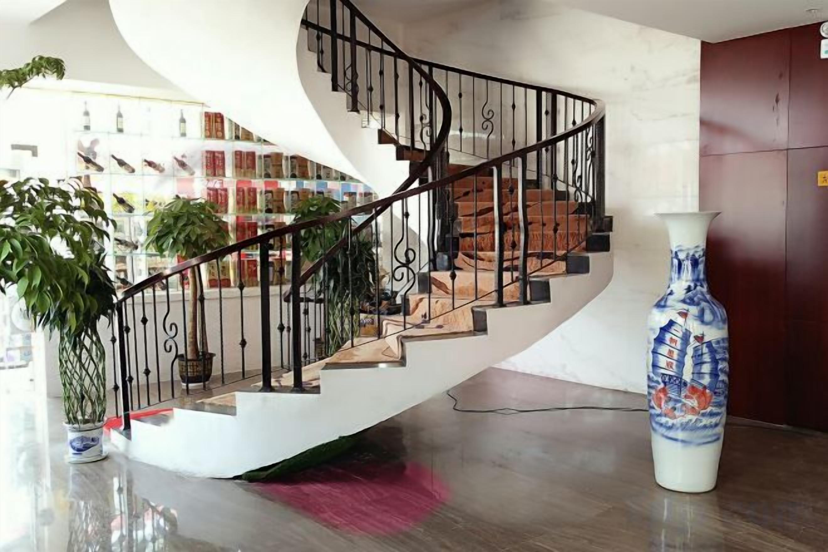 Una escalera de caracol con una pared blanca y un florero sobre una mesa.