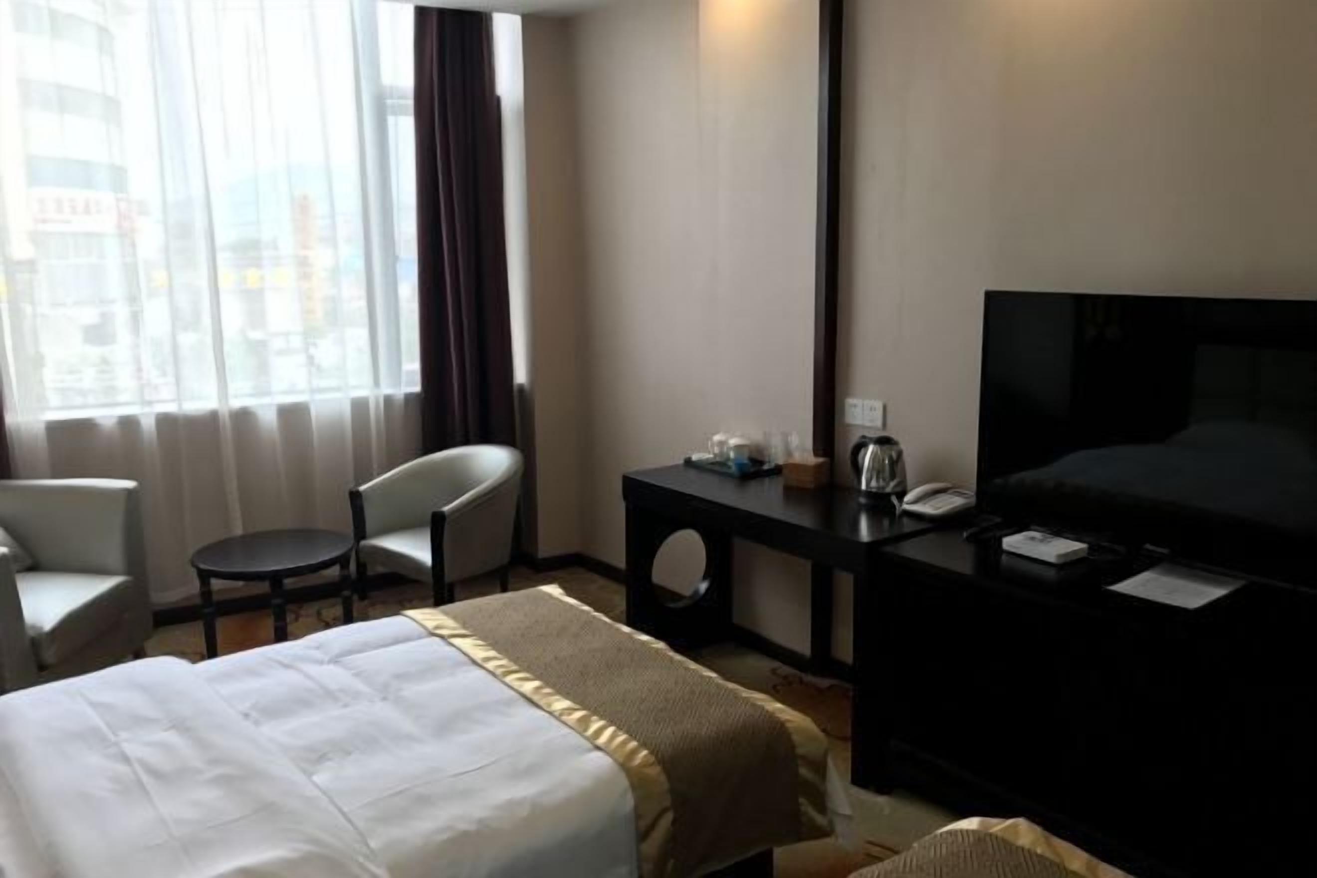 A hotel room with a bed, a desk with a telephone, a chair, and a television.