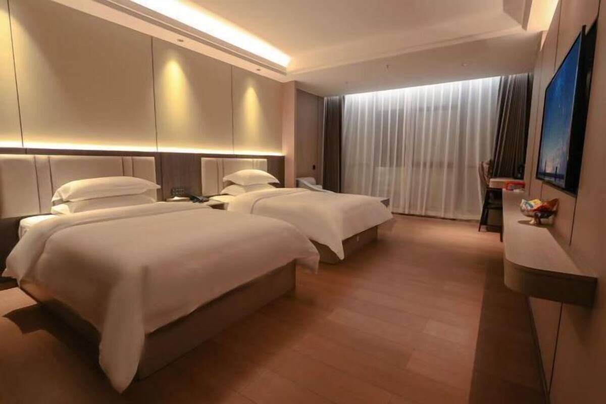 Ein Hotelzimmer mit zwei Betten, einem Flachbildfernseher, einem Schreibtisch und einem großen Fenster mit Vorhängen.