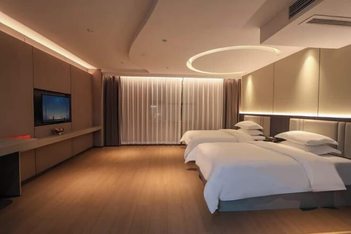 Ein modernes Hotelzimmer mit einem großen Bett, Nachttischen, einem Fernseher und einem fensterbündigen Vorhang.