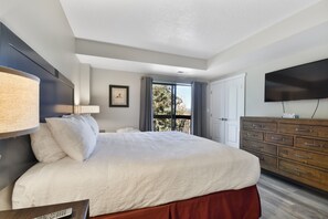 A modern hotel room with a large bed, a TV, a dresser, and a balcony with a view.