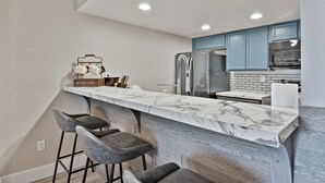 A modern kitchen with a marble countertop, dark blue cabinets, and a stainless steel refrigerator.