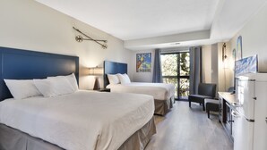 A hotel room with two beds, a desk, a chair, and a refrigerator.
