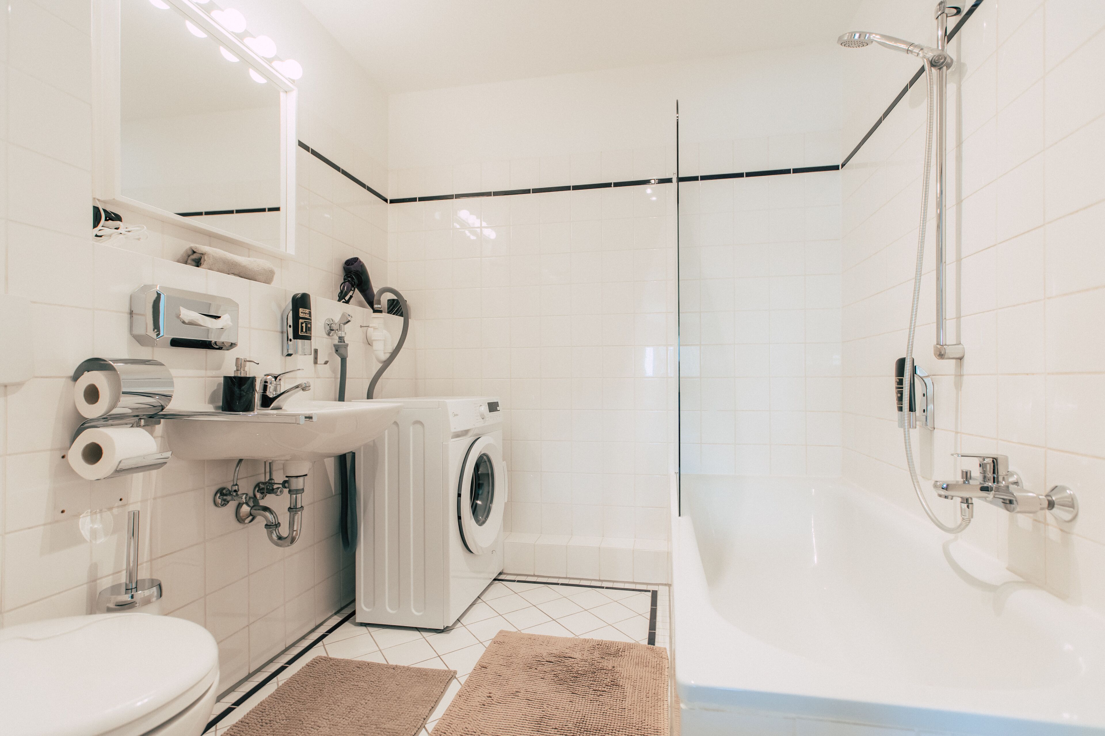 A modern bathroom with a toilet, sink, washing machine, and shower.