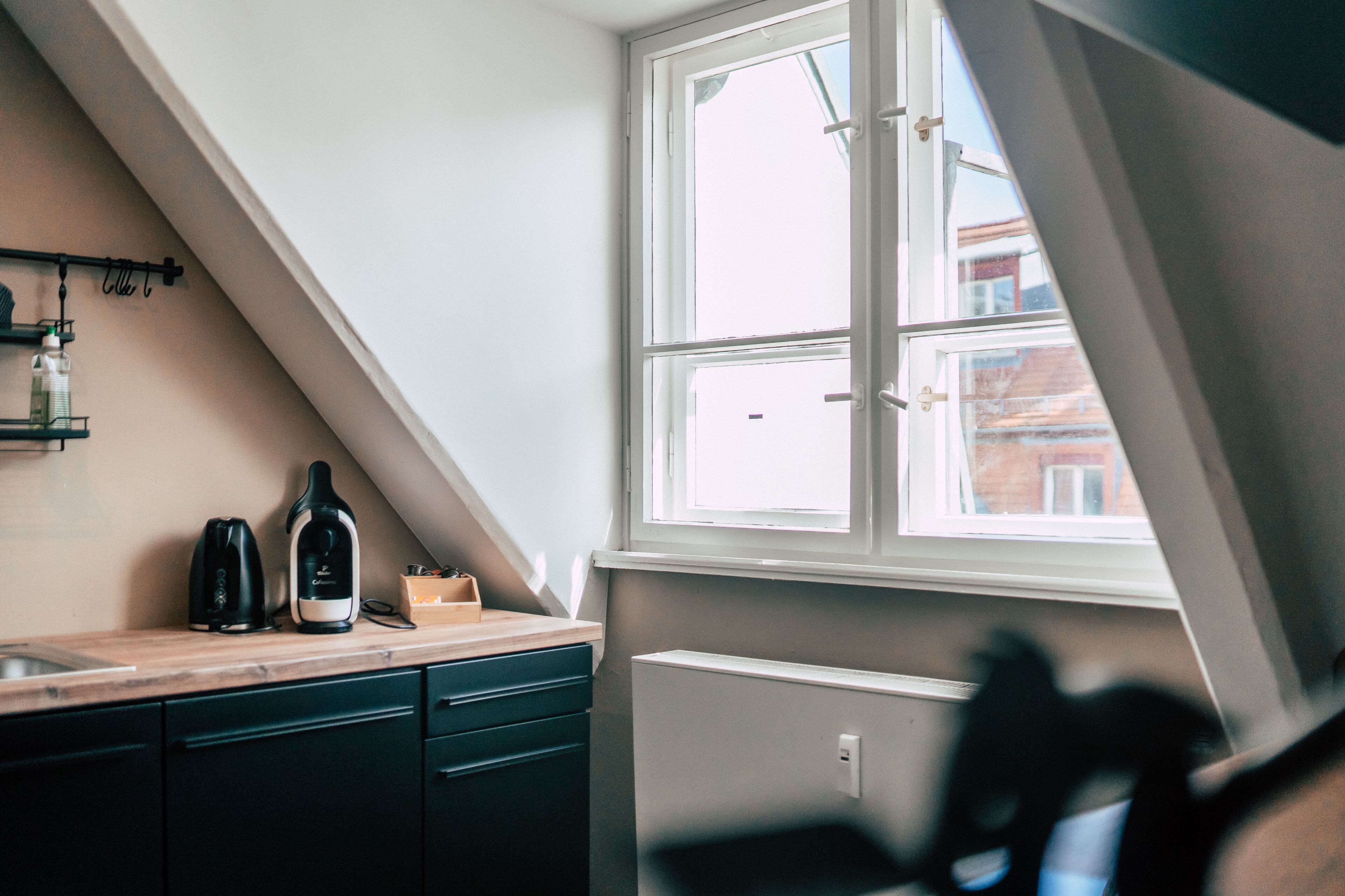 A kitchen with a window, a radiator, and a countertop with a kettle and a bottle.