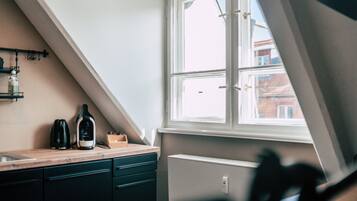 A kitchen with a window, a radiator, and a countertop with a kettle and a bottle.