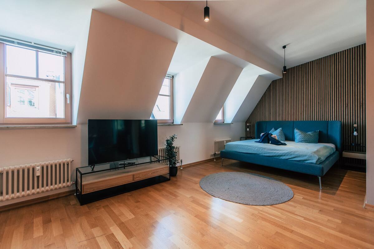 A modern bedroom with a large TV, a bed with blue bedding, and a wooden floor.