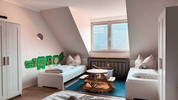 Ein modernes, helles Schlafzimmer mit schrägverdeckter Decke, einem großen Fenster, einem Bett, einem kleinen Tisch und einem Kleiderschrank.