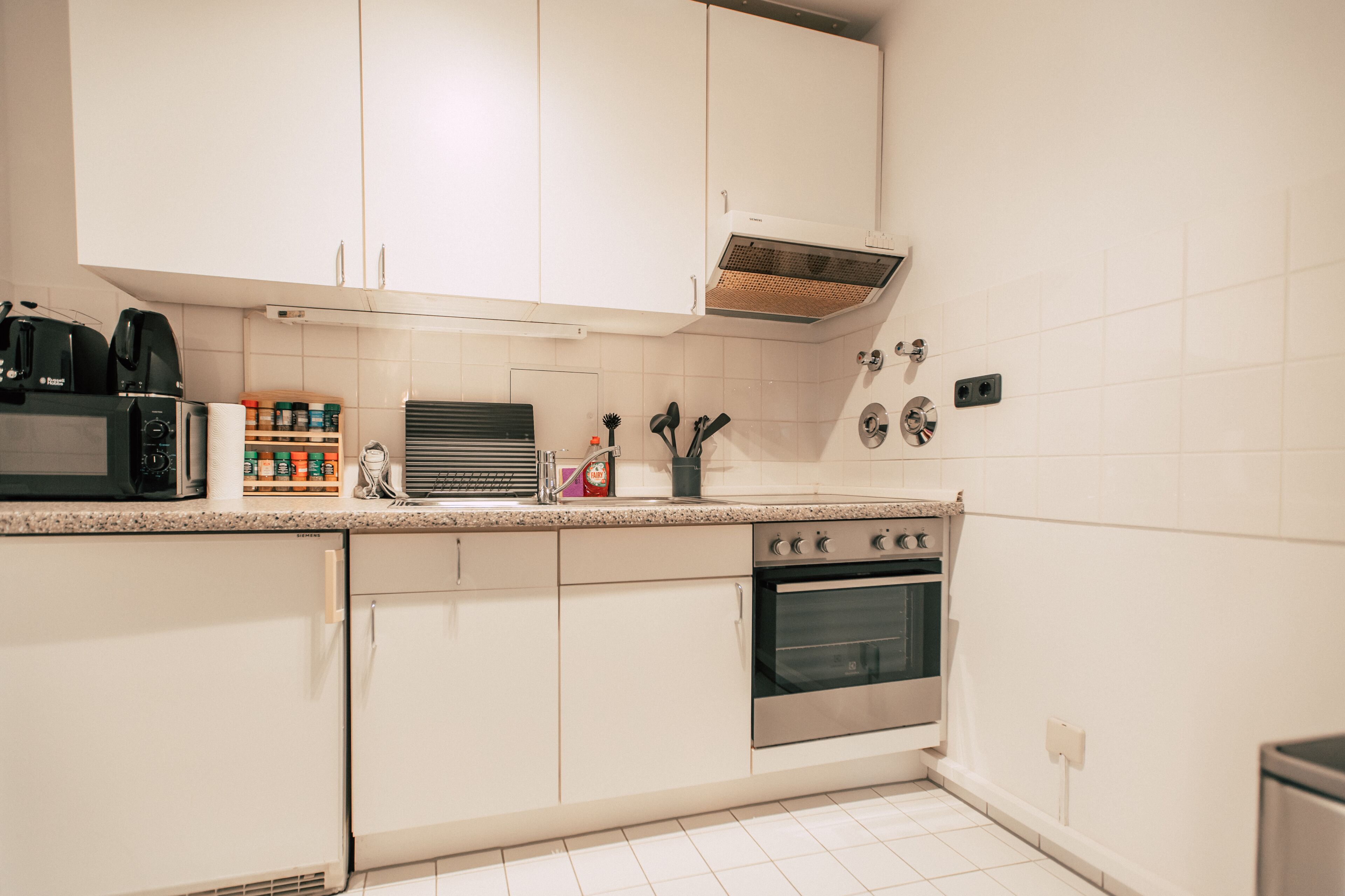 Une cuisine avec des meubles blancs, une cuisinière et un four à micro-ondes.