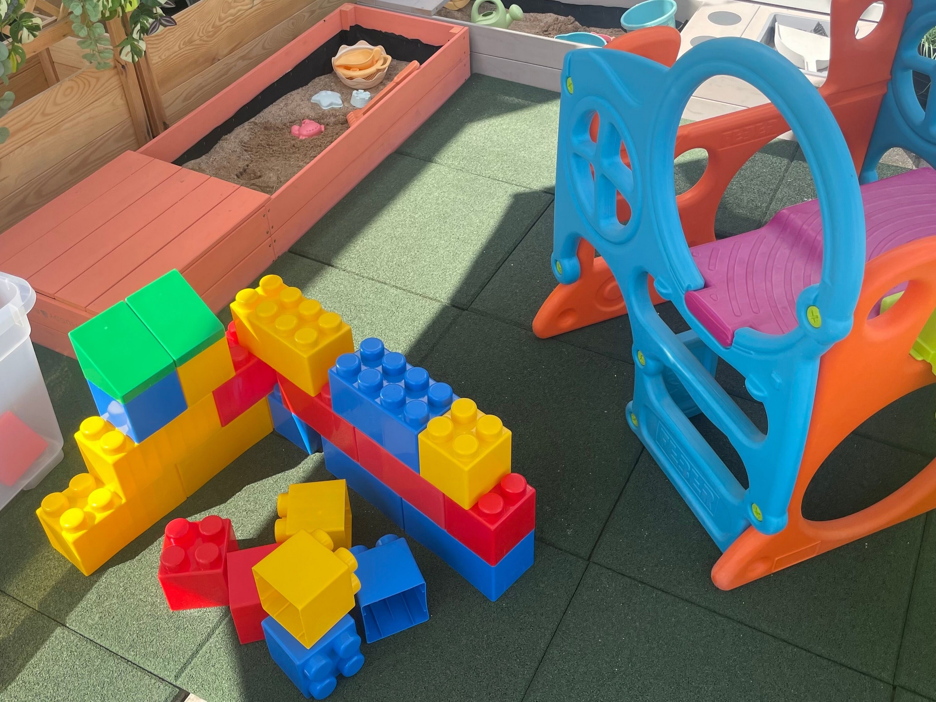 A play area with a sandbox, colorful plastic toys, and a blue and orange plastic chair.