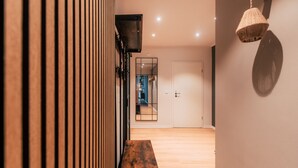 Un corridoio con listelli di legno, una panca in legno, uno specchio, una porta e una lampada in fibra naturale.