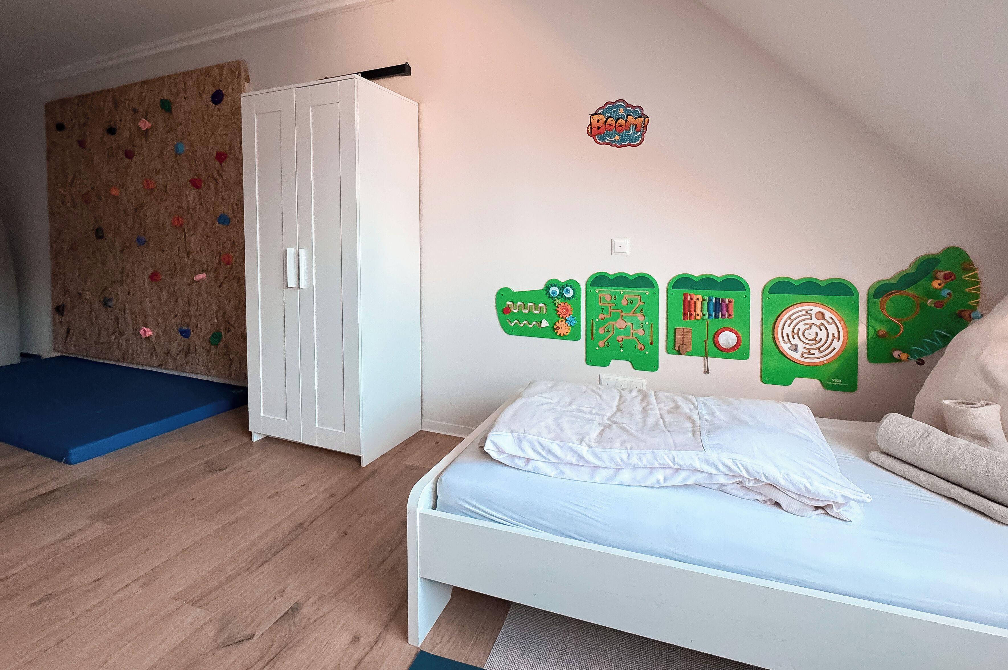 Un dormitorio con cama blanca, pared de escalada y decoraciones educativas en la pared.