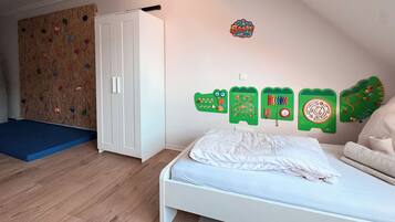 Un dormitorio con cama blanca, pared de escalada y decoraciones educativas en la pared.