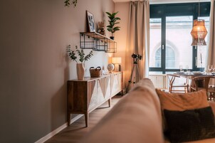 Una sala de estar acogedora con un sofá, una consola de madera, una lámpara y una ventana con cortinas.