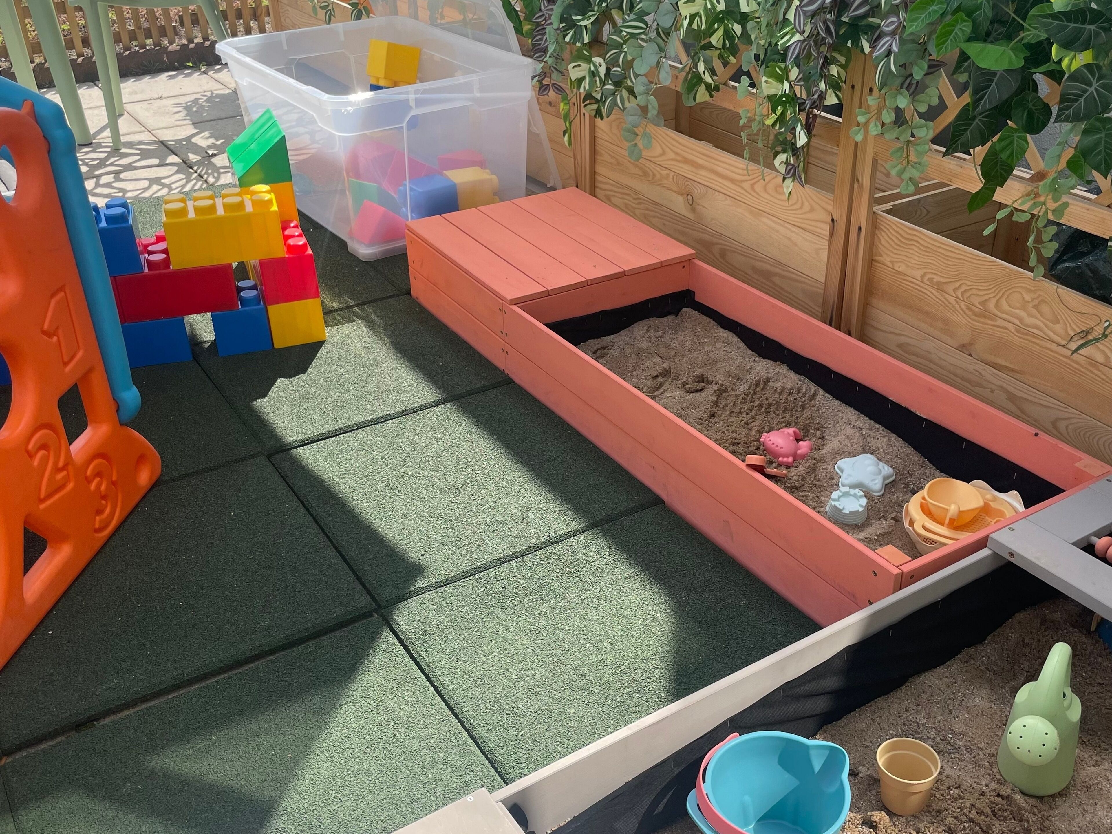Un espace de jeux pour enfants avec un bac à sable, des boîtes de rangement en plastique et des blocs de construction colorés.
