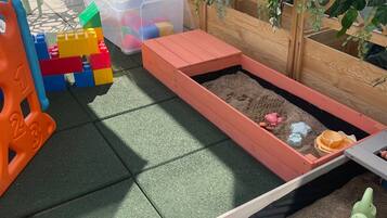 Un espace de jeux pour enfants avec un bac à sable, des boîtes de rangement en plastique et des blocs de construction colorés.