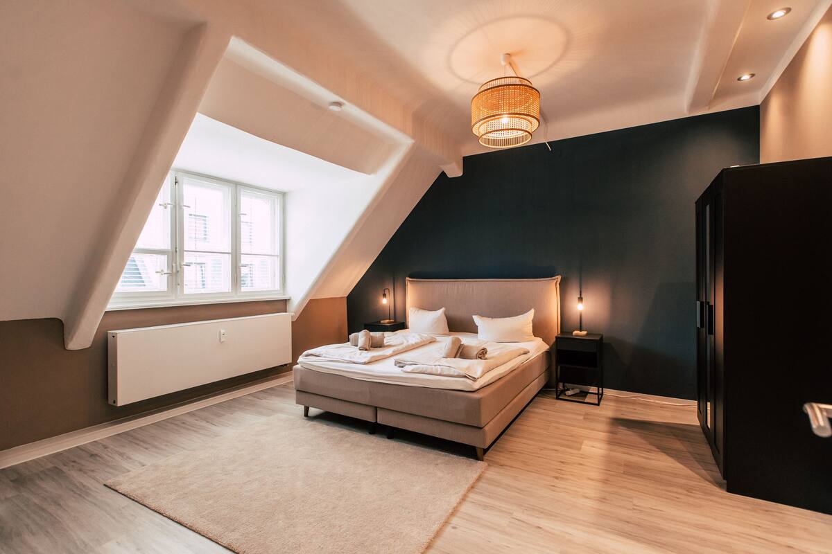 A modern bedroom with a large bed, a ceiling light fixture, a nightstand, and a radiator.