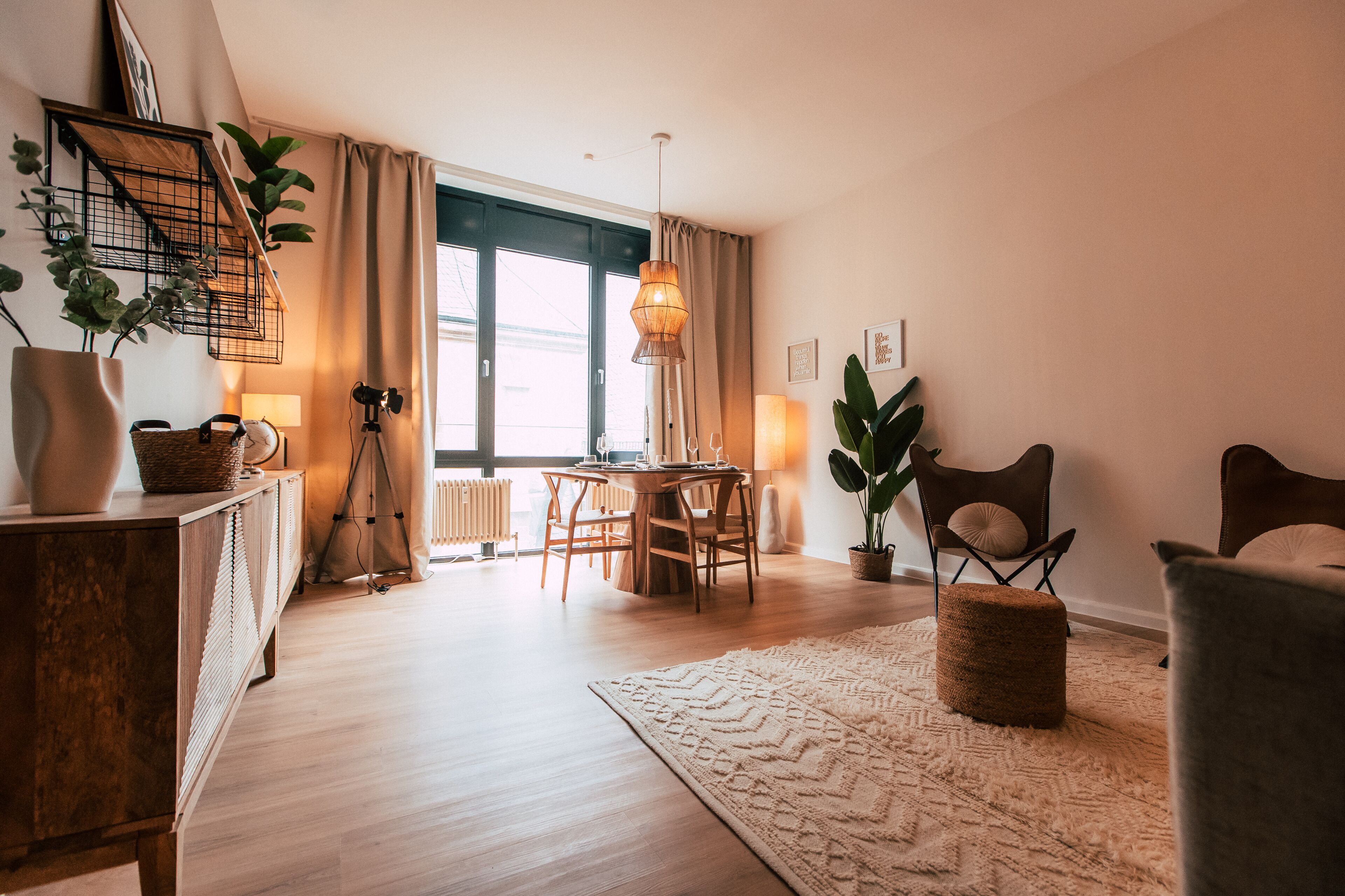 Un salon moderne avec un plancher en bois, un coin repas avec une table et des chaises, une grande fenêtre avec des rideaux et un luminaire suspendu.