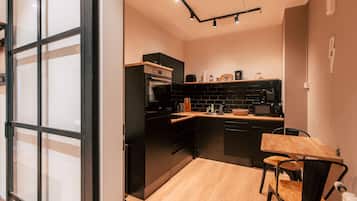 A compact kitchen with black cabinets, a wooden dining table, and a black chair.