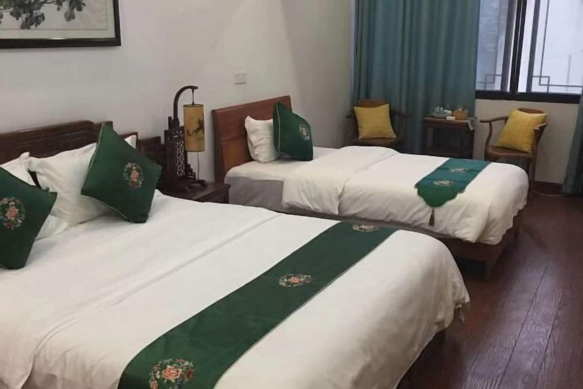 A hotel room with two beds, each with green bedspreads and pillows, a nightstand with a lamp, and a window with curtains.