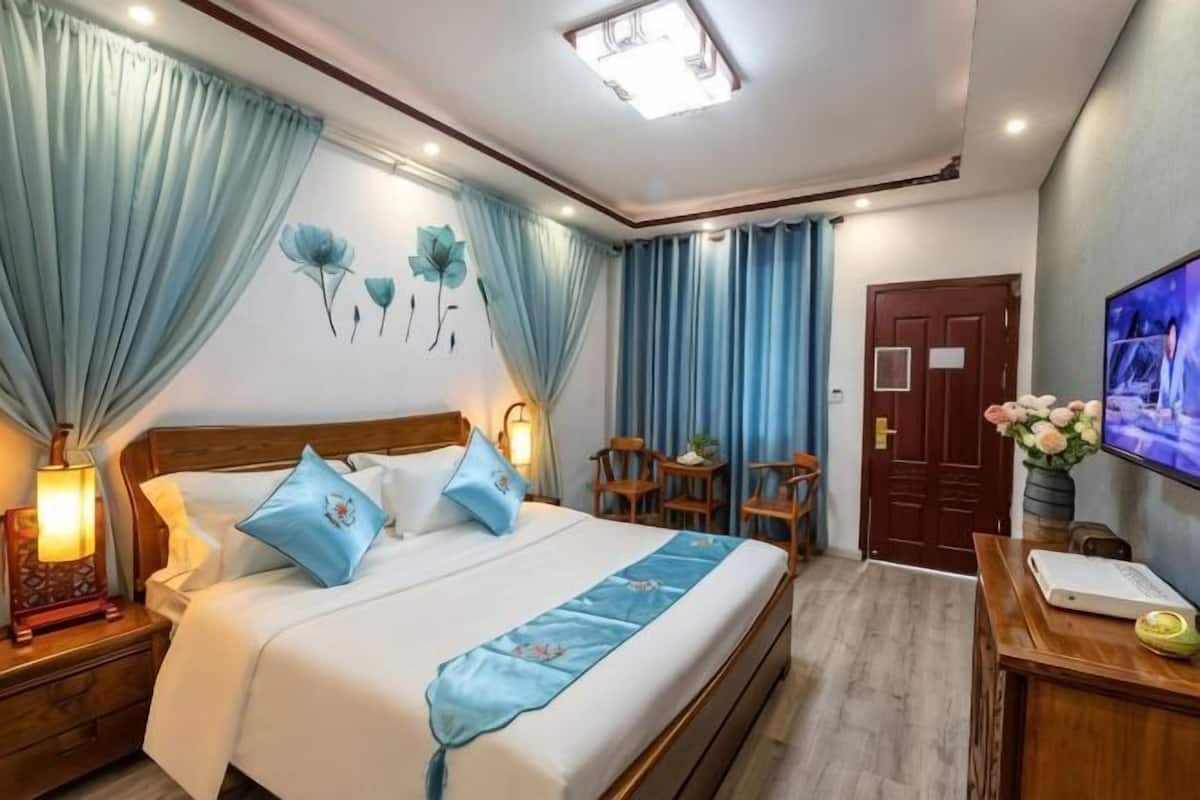 A bedroom with a bed, curtains, a TV, a desk, and a chair.