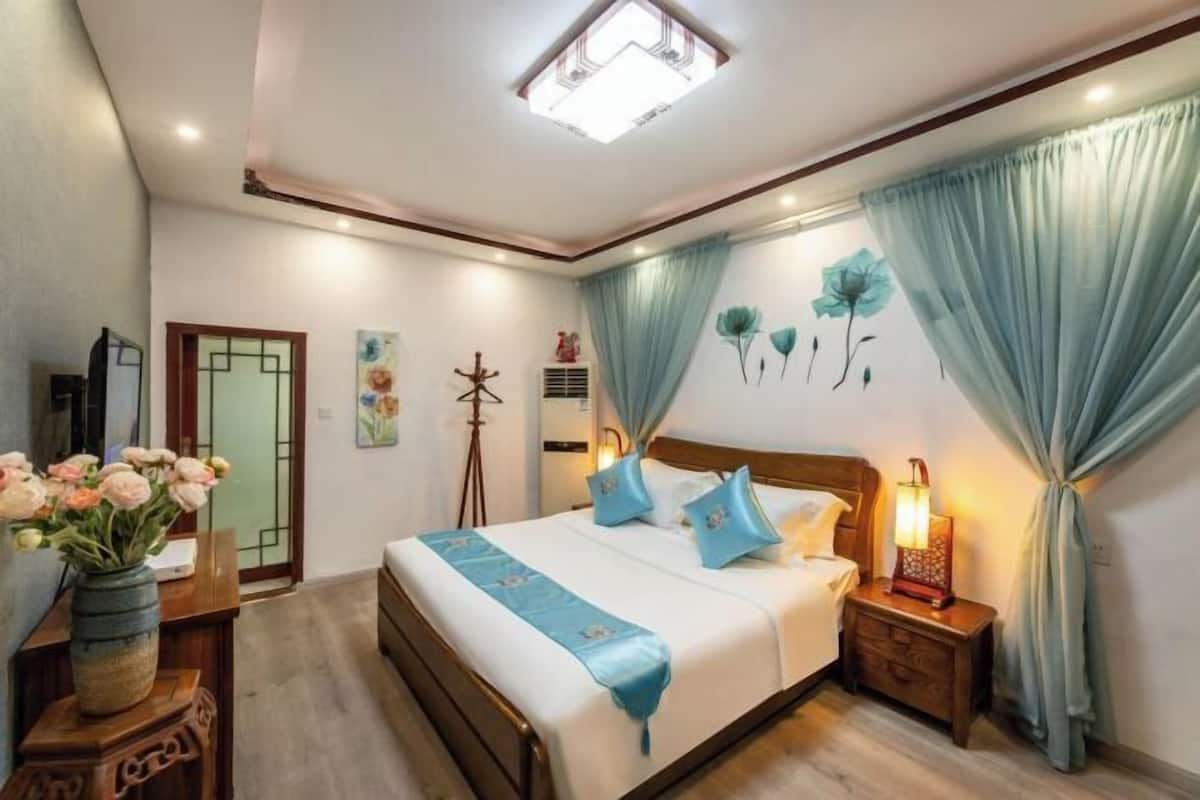 A bedroom with a bed, bedside tables, a nightstand, a desk with a vase of flowers, and a wall with a painting.