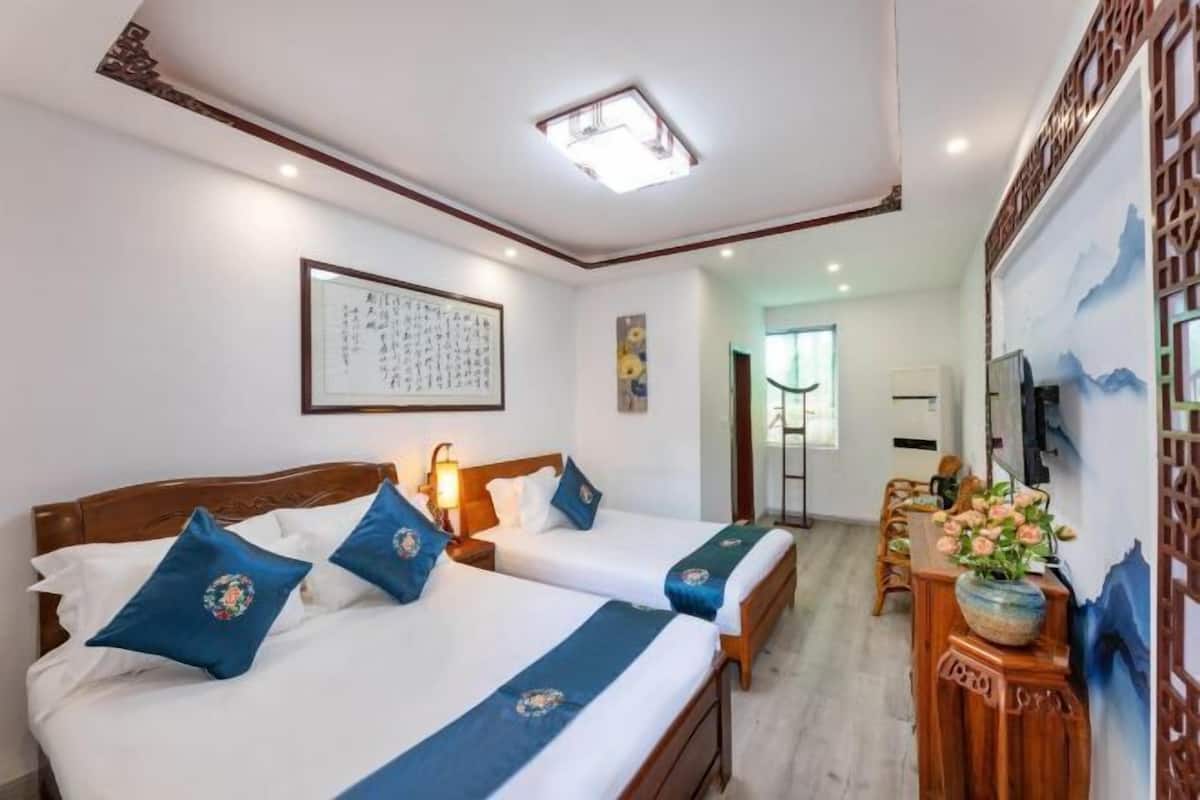 A hotel room with two beds, a desk, a chair, a TV, and a painting on the wall.