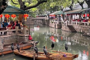 Ein traditioneller Wasserweg mit Booten und hölzernen Brücken, umgeben von Bäumen und historischen Gebäuden.