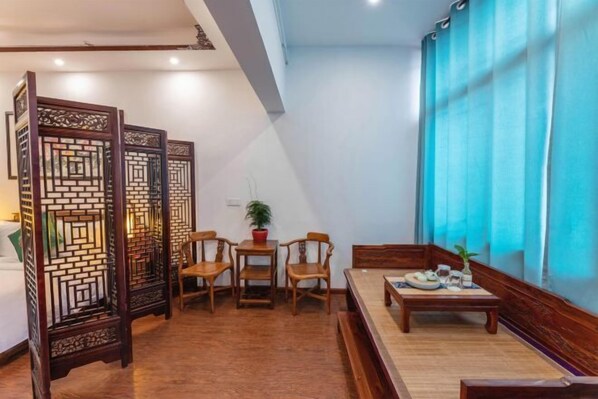 Quarto em estilo tradicional com divisória de madeira, área de jantar com mesa e cadeiras, e uma grande janela com cortinas azuis.