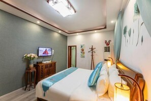 Quarto de hotel com cama, televisão, uma pequena mesa com um vaso de flores e uma luminária na parede.