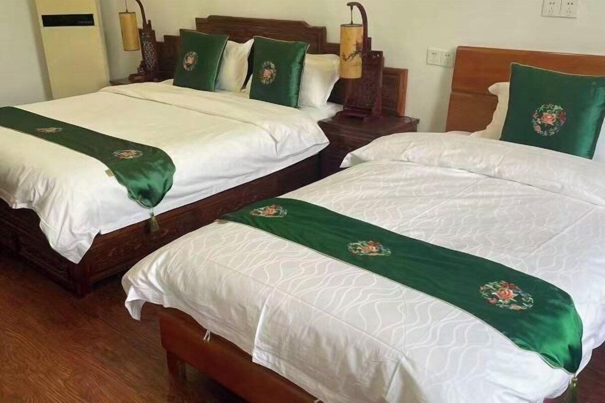 Two double beds with wooden frames and green bedspreads, a wooden nightstand with a lamp, and a wooden headboard with a floral design.