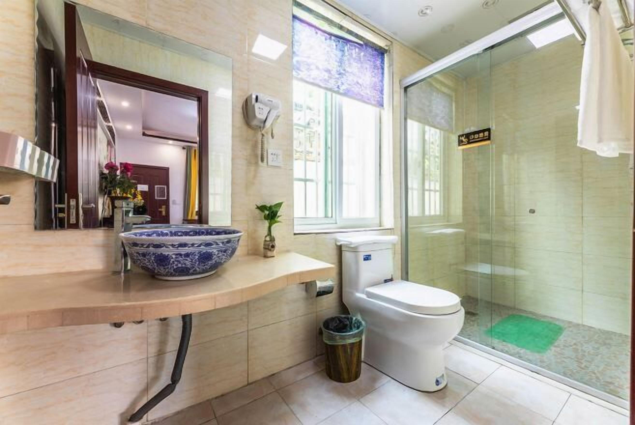 A modern bathroom with a large blue ceramic sink, a toilet, and a glass shower enclosure.