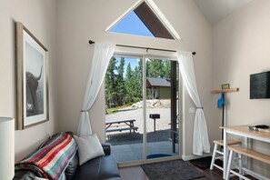 Una habitación con un amplio ventanal corredero que da a un espacio al aire libre, un sofá de cuero negro, una pequeña mesa de madera y un cuadro en la pared.