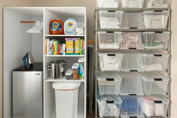 Una cocina equipada con refrigerador, estufa y diferentes utensilios. También hay estantes con libros y contenedores de almacenamiento.
