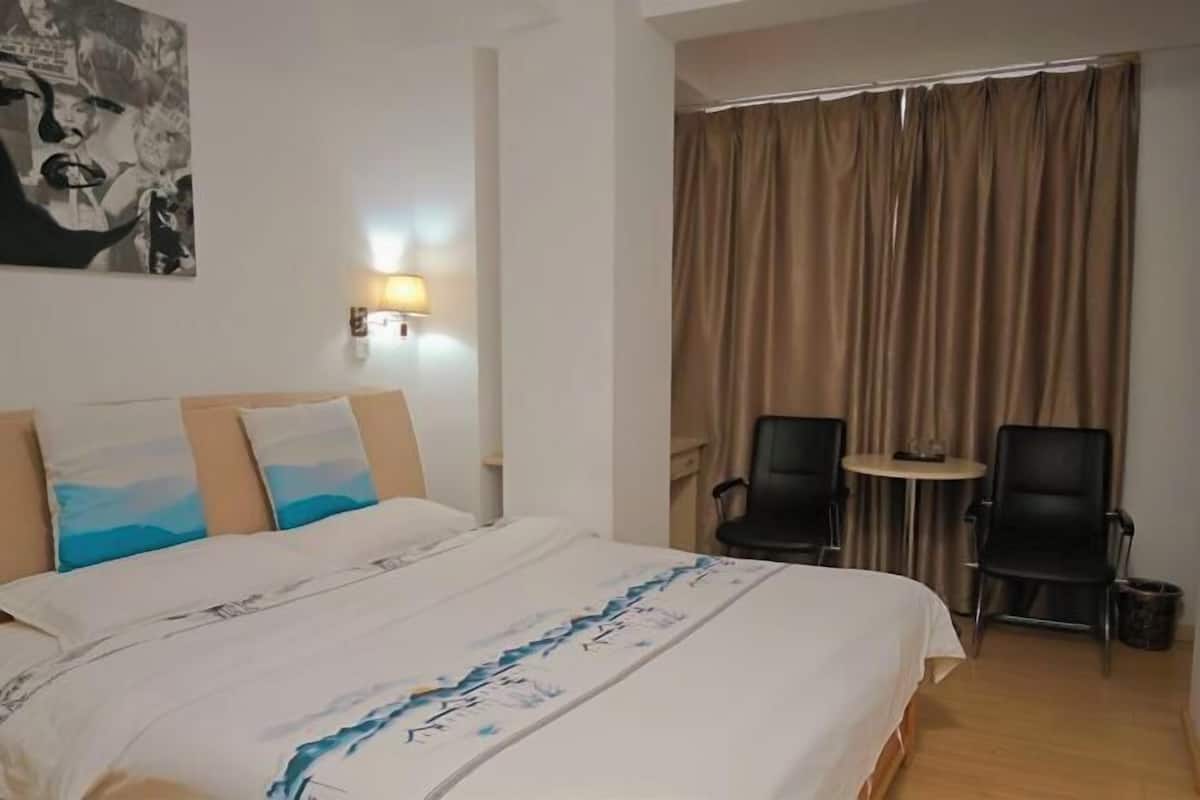 A hotel room with a bed, two chairs, a small table, and a curtain.