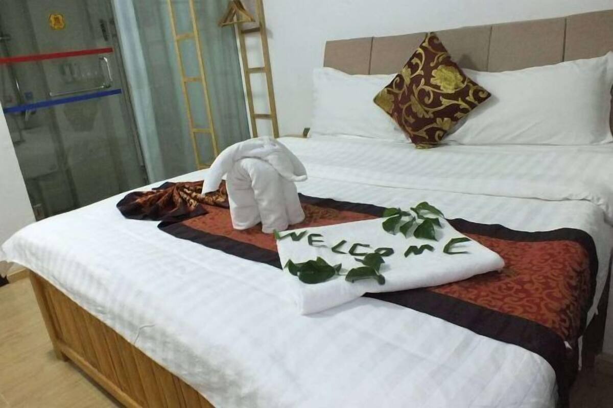 Two beds with white bedspreads, a welcome pillow, and a brown jacket adorn this inviting space.