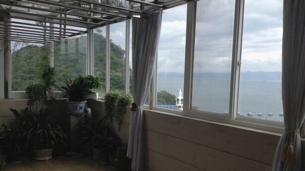 Una habitación con ventanas amplias, vista a un cuerpo de agua y varias plantas en macetas.