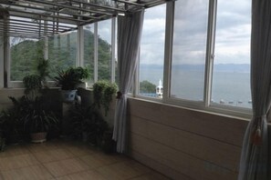 A room with a large window overlooking a body of water, potted plants, and a wooden floor.