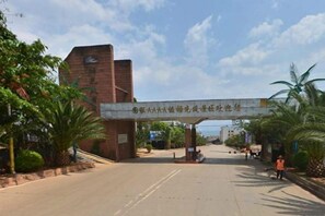 A building entrance with a sign, a paved road, and some greenery.