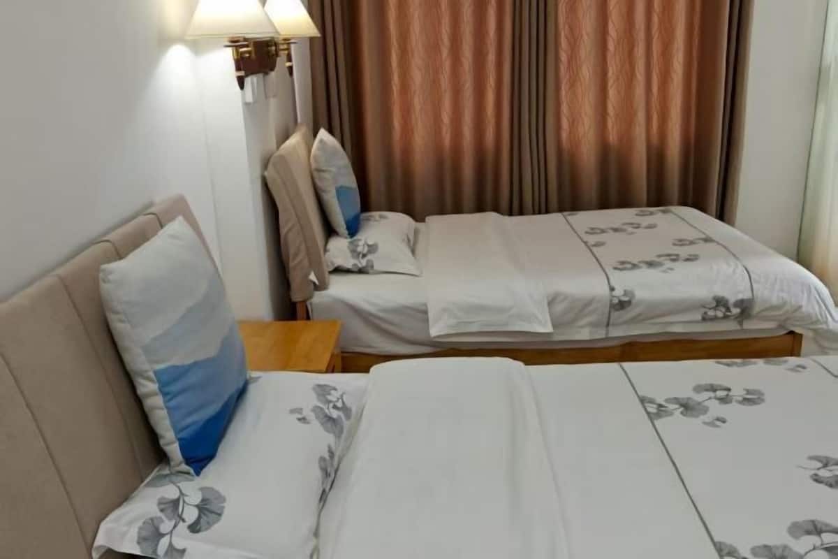 A hotel room with two beds, a nightstand, a lamp, and a window with curtains.