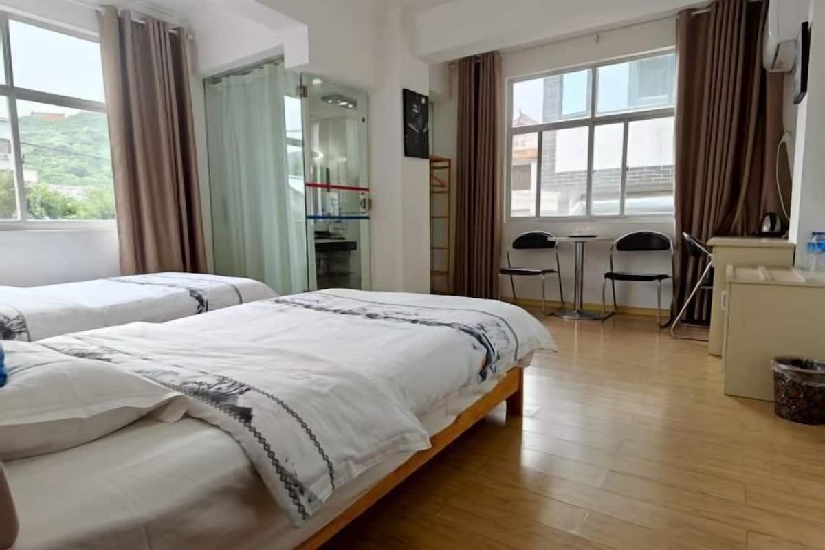 A hotel room with two beds, a desk, chairs, a small table, and a window.