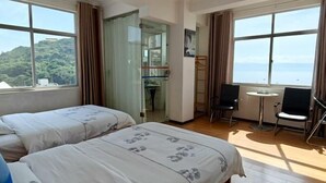 Habitación de hotel con dos camas, una mesita, dos sillas y ventanas amplias con vista al mar.