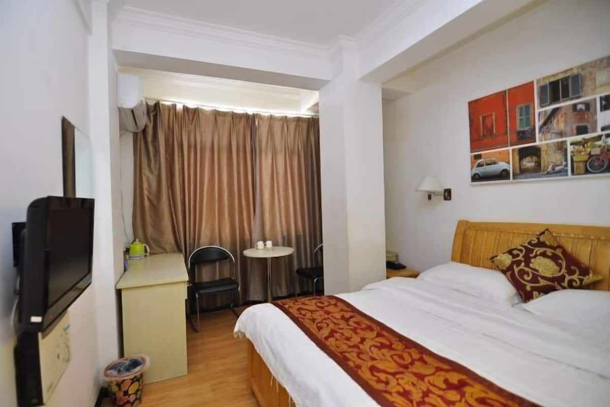 A hotel room with a bed, a desk, a chair, a small table, a television, and a window with curtains.