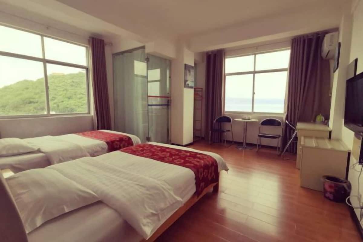 A hotel room with two beds, a desk, a chair, and a TV.