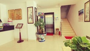 Zona de recepción con mostrador, diplomas enmarcados, una planta en maceta y una escalera que lleva a un ascensor.