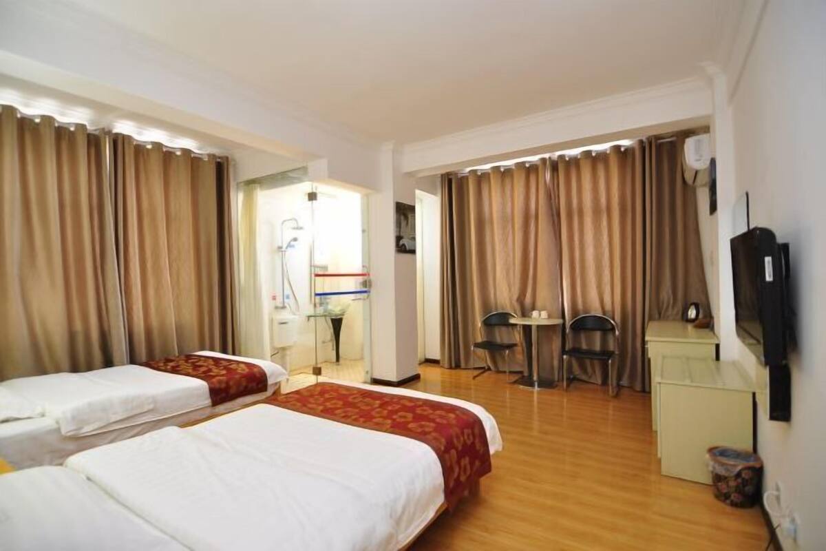 Two single beds with white linens and red bedspreads, a desk, and a mounted television.