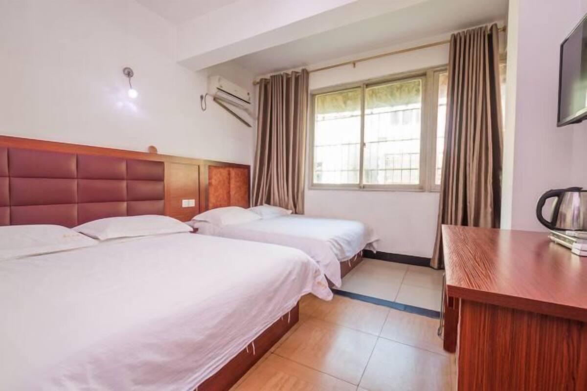 A hotel room with two beds, a wooden headboard, a window with curtains, a wooden desk, and a television.