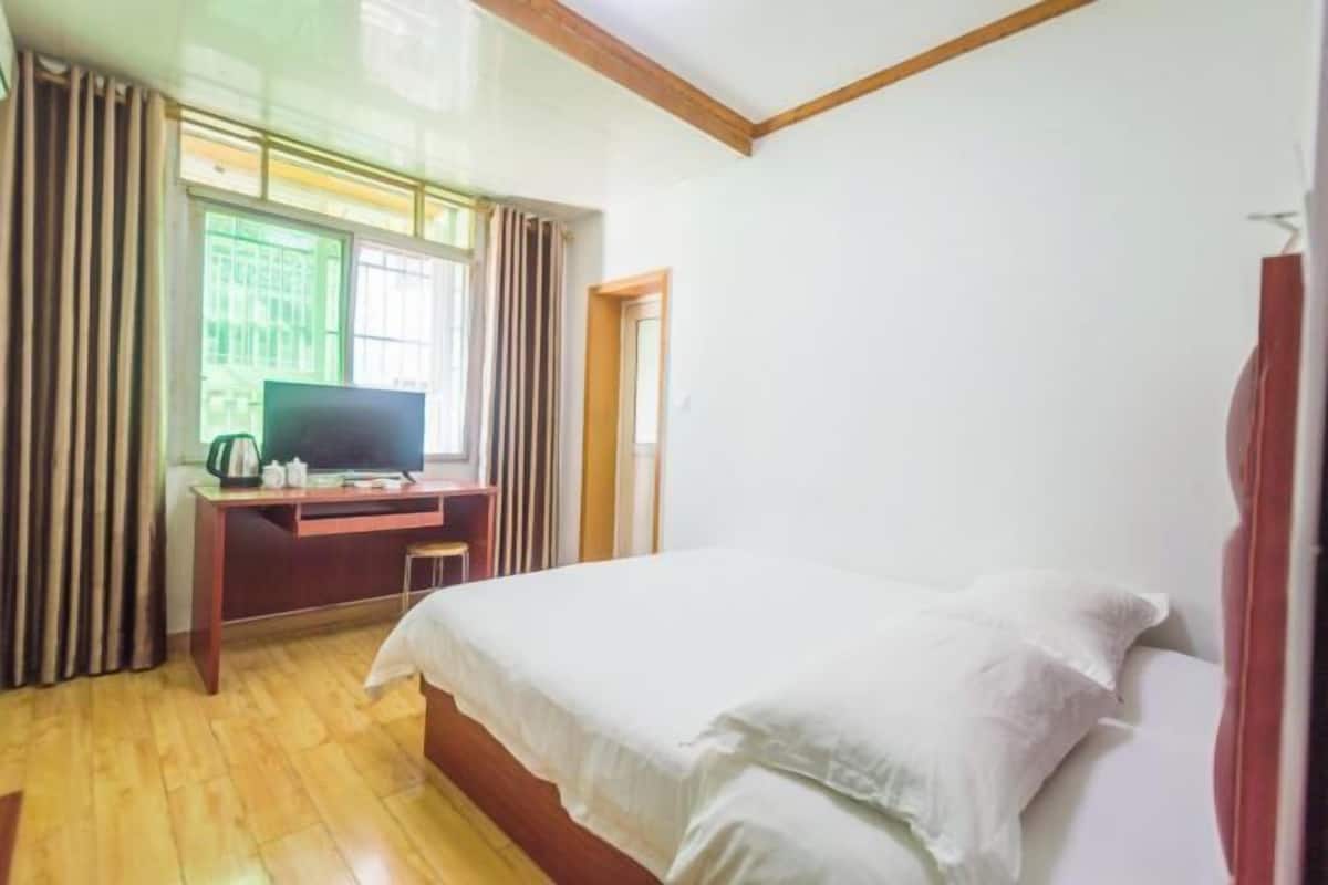 A bedroom with a bed, a desk, a television, and a window with curtains.