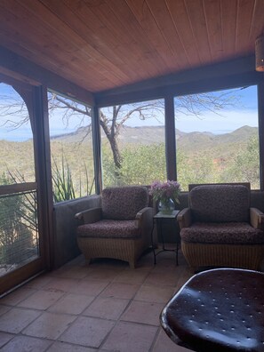 Relax in this serene outdoor space with a view of the surrounding mountains, featuring a comfortable seating area with a vase of fresh flowers.