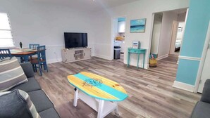 Una sala de estar con sofá, una mesa de centro, televisión y un comedor con sillas.